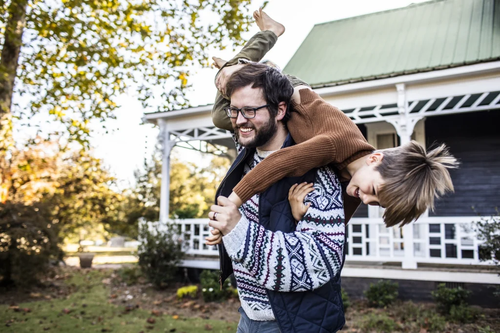 Country-Bank-father-swinging-son-over-his-back-outside-their-new-home