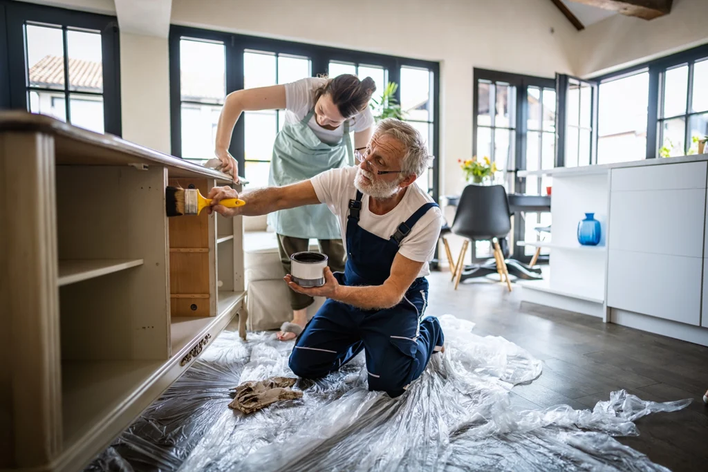 Country-Bank-man-and-woman-staining-furniture-in-room-with-dropcloth-on-floor