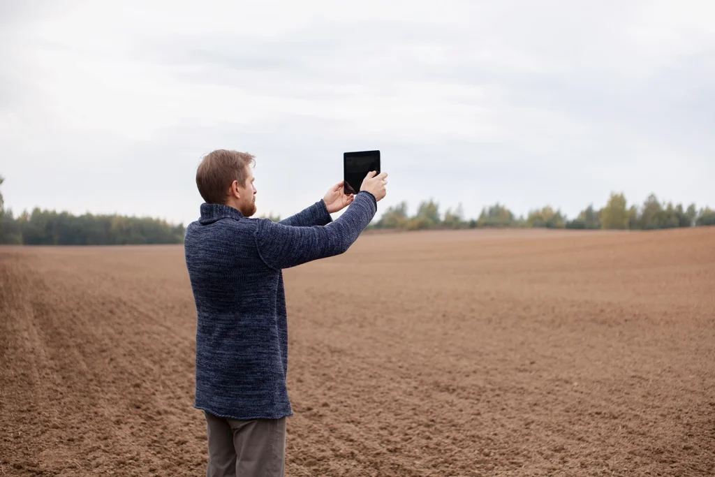 Country-Bank-man-in-blue-sweater-holding-up-ipad-to-a-dirt-lot