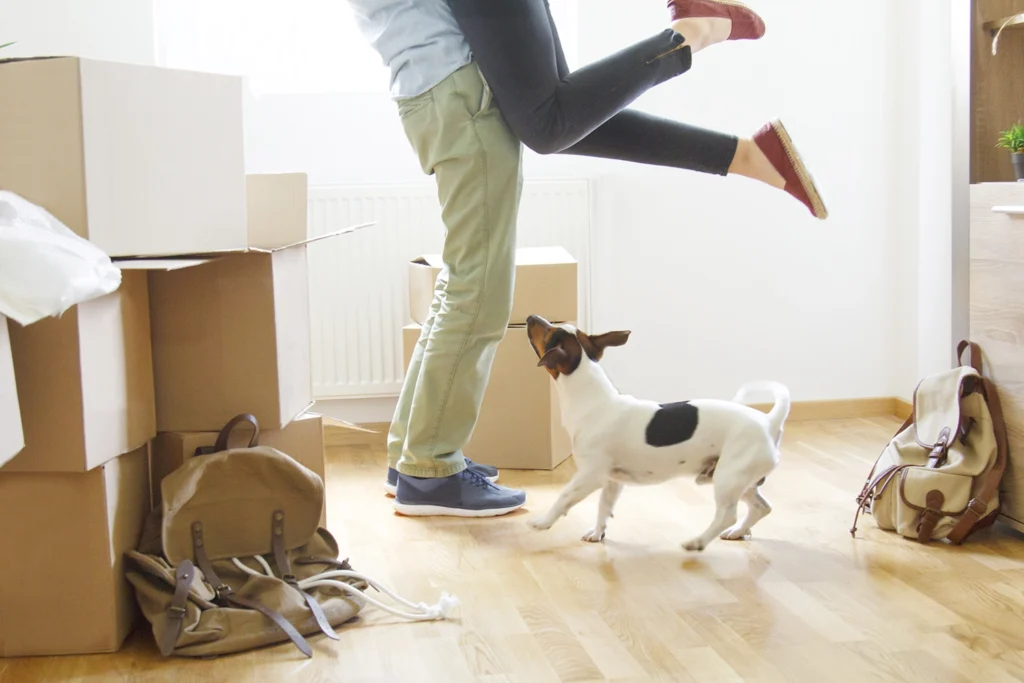 Country-Bank-man-lifting-woman-up-in-hug-with-dog-and-boxes-in-new-home