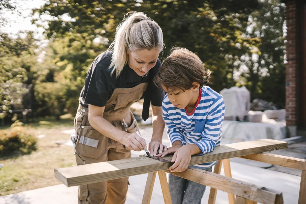 Country-Bank-woman-in-construction-clothes-working-with-son-to-measure-plank