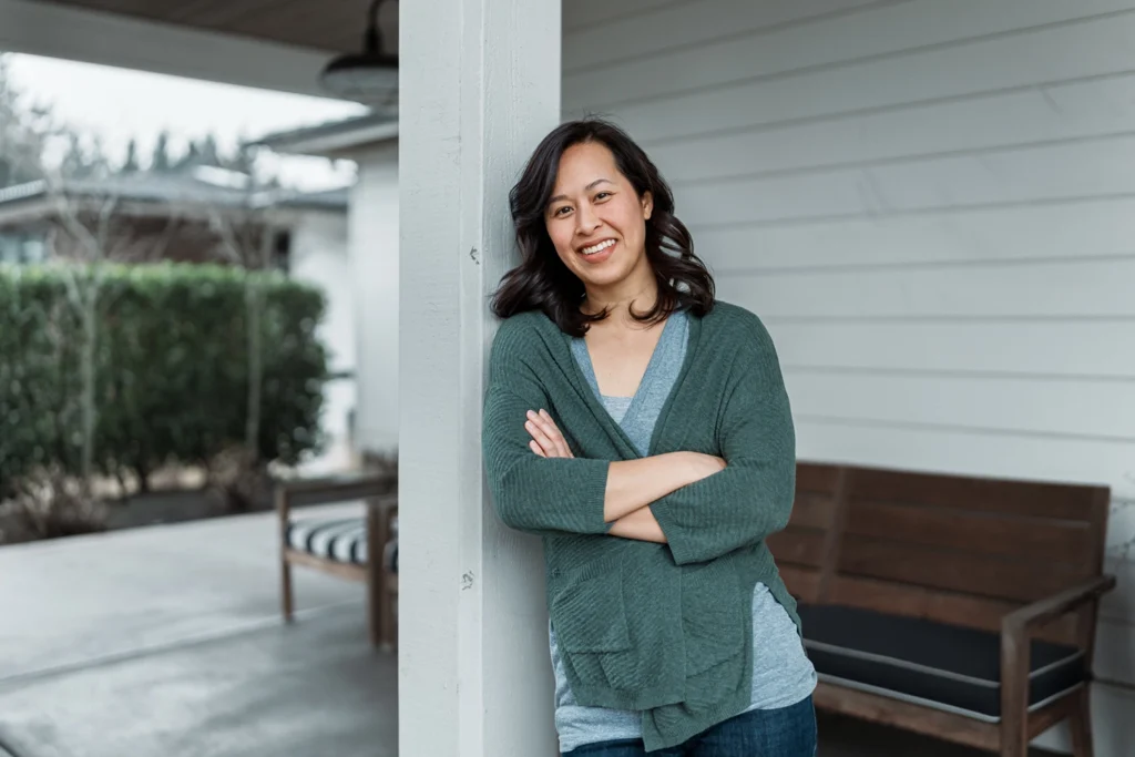 Country-Bank-woman-leaning-against-porch-column-of-new-home-with-arms-folded