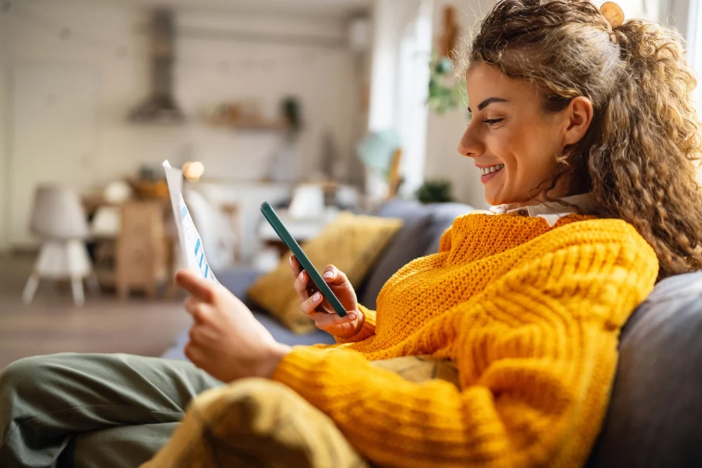 Country-Bank-woman-on-couch-reading-loan-papers-and-looking-at-phone
